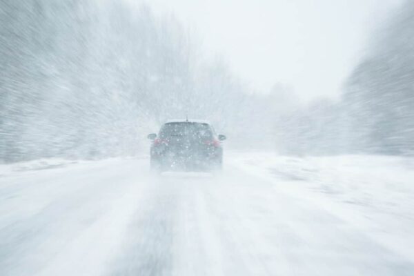 A car drives away from the camera down a snow-covered road
