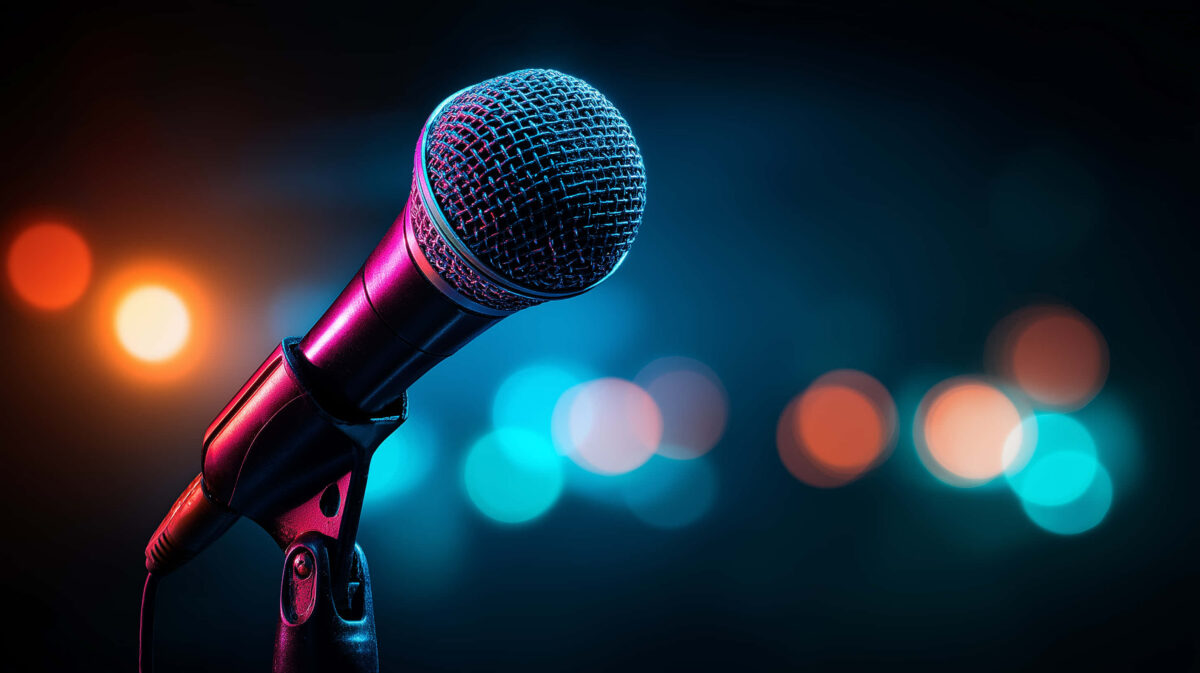 A microphone on a mic stand in the foreground, with blurred colored lights behind it.